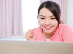 Woman with dark hair in pink shirt looking at a laptop computer