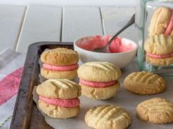 Cookies on a metal tray some sandwiched with pink frosting